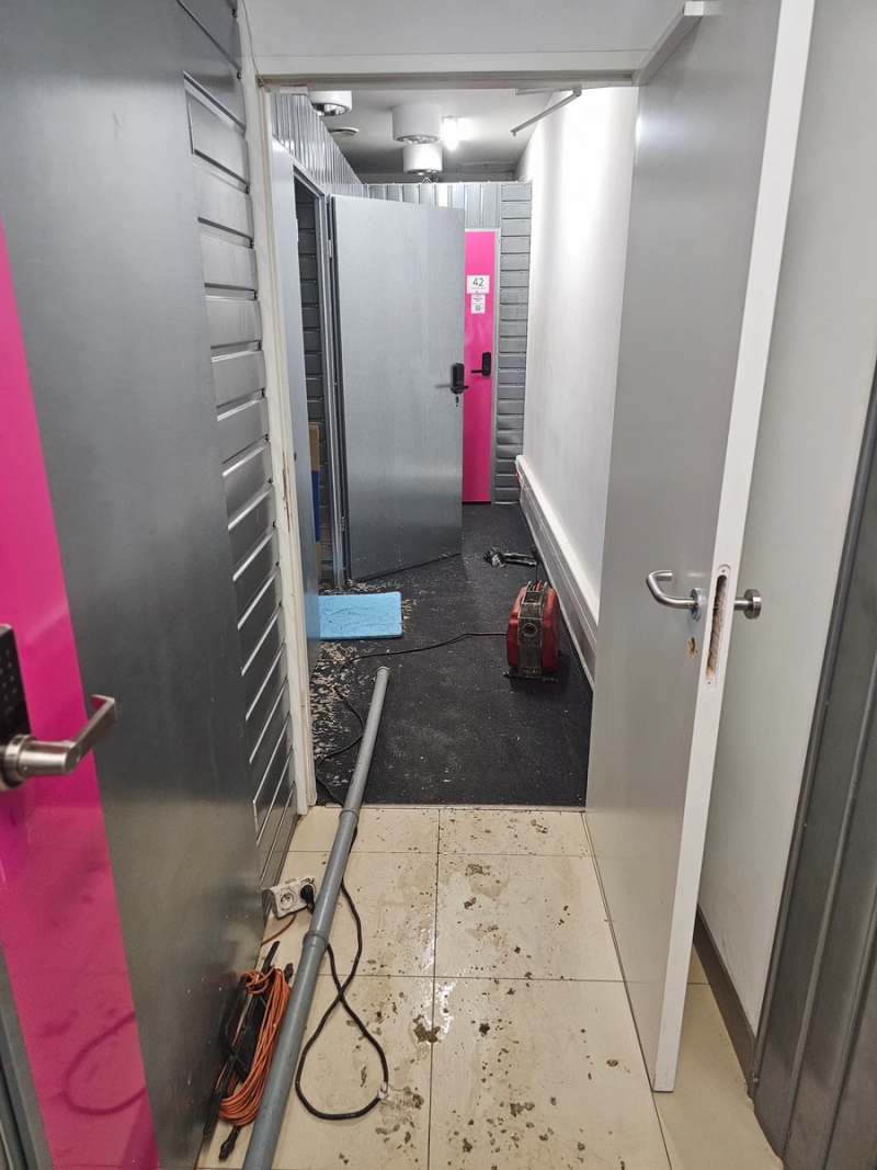 Zalana podłoga w magazynach lokatorskich po awarii kanalizacji – ślady ścieków wybijających spod pionu z rewizją