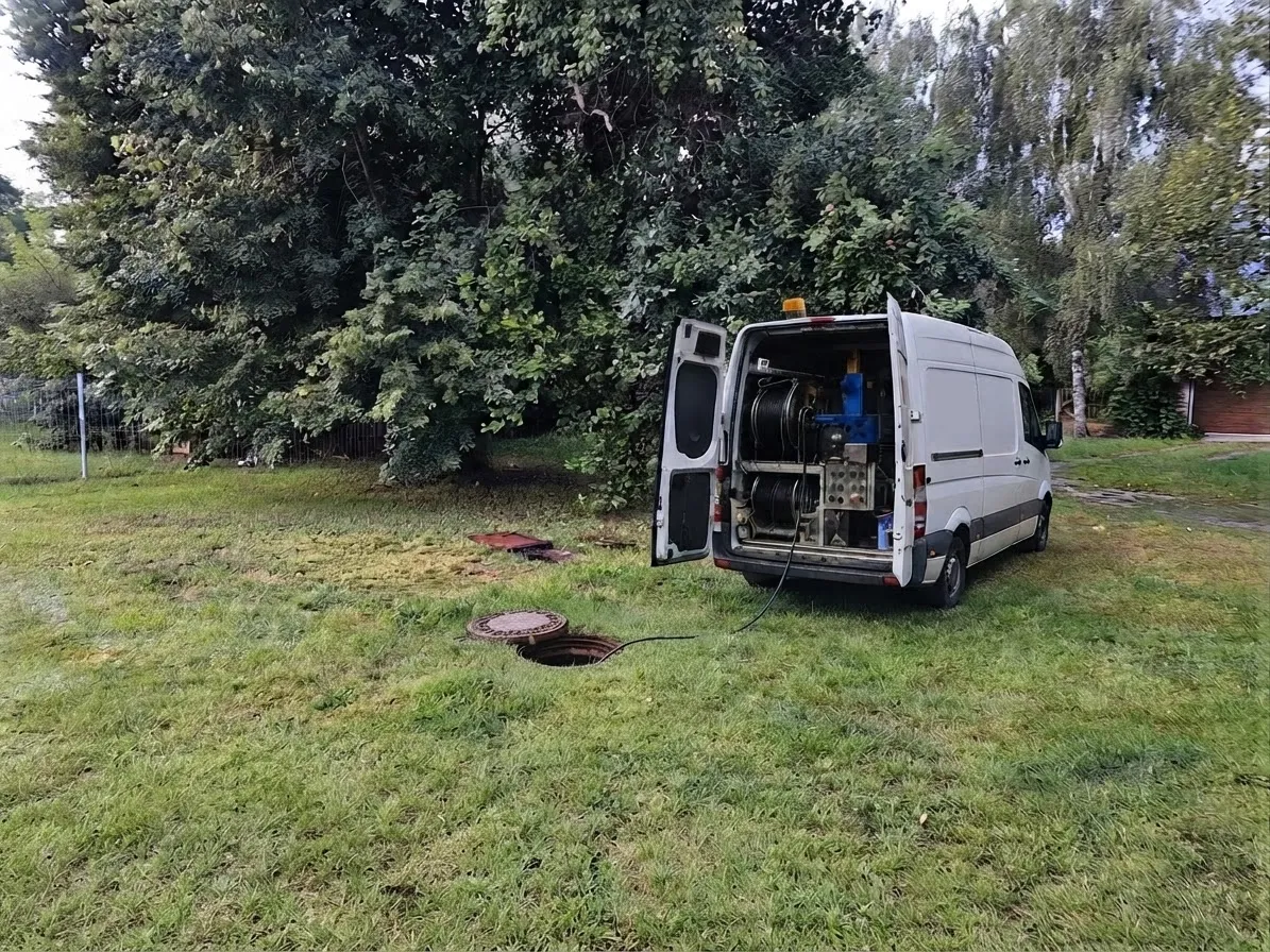 Samochód z zabudową WUKO na trawniku przy domu jednorodzinnym – wąż ciśnieniowy wprowadzony do studzienki rury biegnącej do szamba