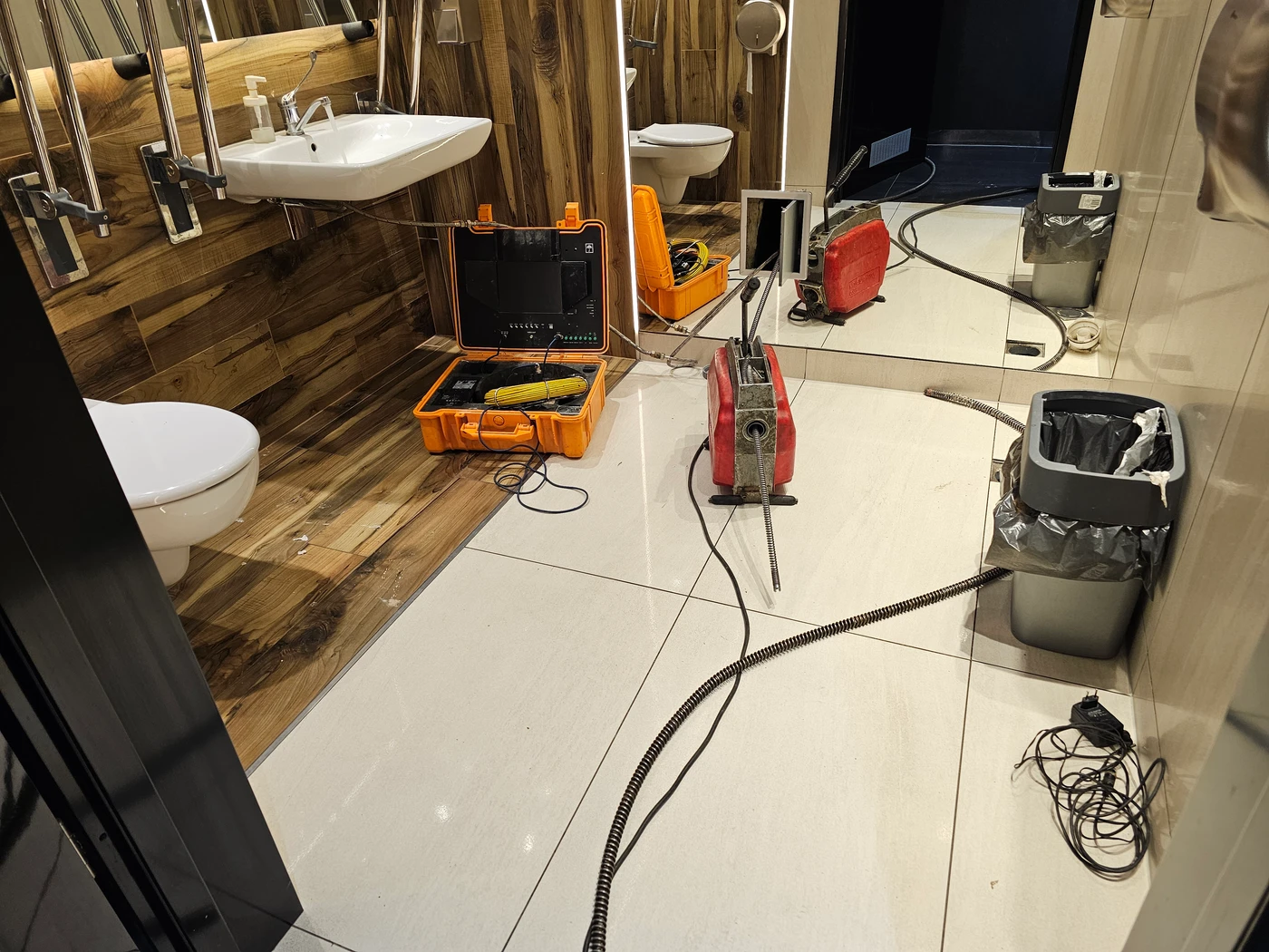 Otwarte drzwiczki rewizyjne w ścianie z lustrem i elektryczna sprężyna ze spiralą wprowadzoną do pionu kanalizacyjnego